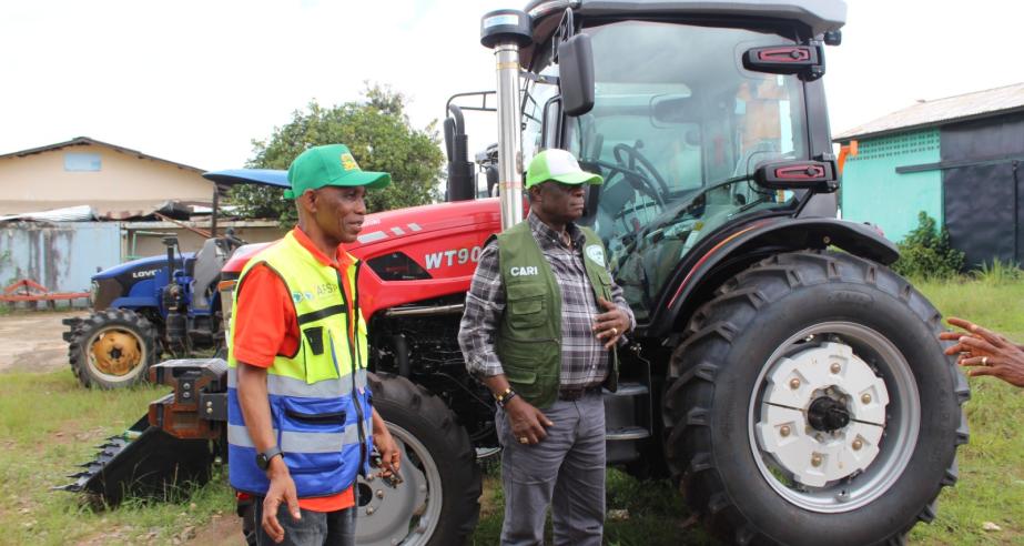 Dr. Arthur Bob Karnuah, Director General of CARI, and Daniel Wiagbe, National Coordination Officer of the SADFONS Project, pose together during the official handover of advanced 90‑horsepower tractor accompanied by multiple implements, power tillers, and motorized sprayers.