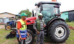 Dr. Arthur Bob Karnuah, Director General of CARI, and Daniel Wiagbe, National Coordination Officer of the SADFONS Project, pose together during the official handover of advanced 90‑horsepower tractor accompanied by multiple implements, power tillers, and motorized sprayers.